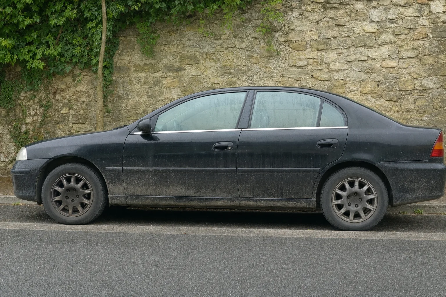 Lavage extérieur de voiture à domicile à Caen — flanc avant intervention : carrosserie poussiéreuse, bas de caisse sale, jante noircie.