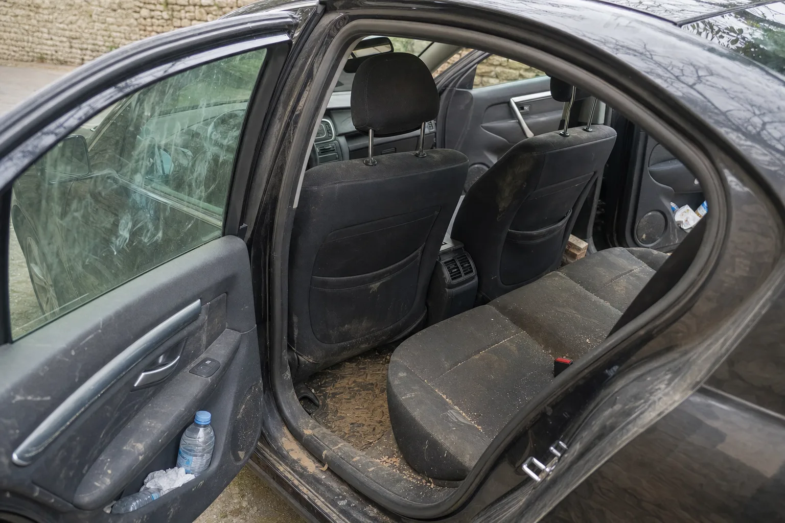 Nettoyage intérieur de voiture à domicile à Caen — habitacle avant intervention : sièges en tissu tachés, tapis maculés, déchets au sol.