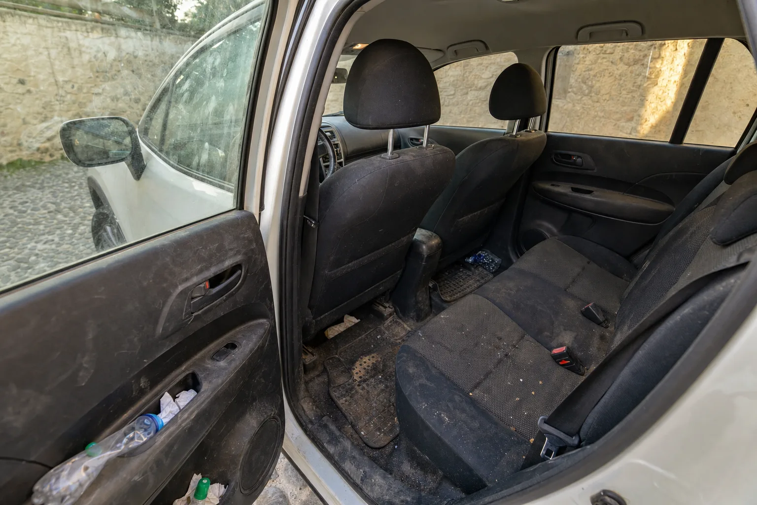 Nettoyage intérieur de voiture à domicile à Toulouse — habitacle avant intervention : sièges en tissu tachés, tapis maculés, déchets au sol.