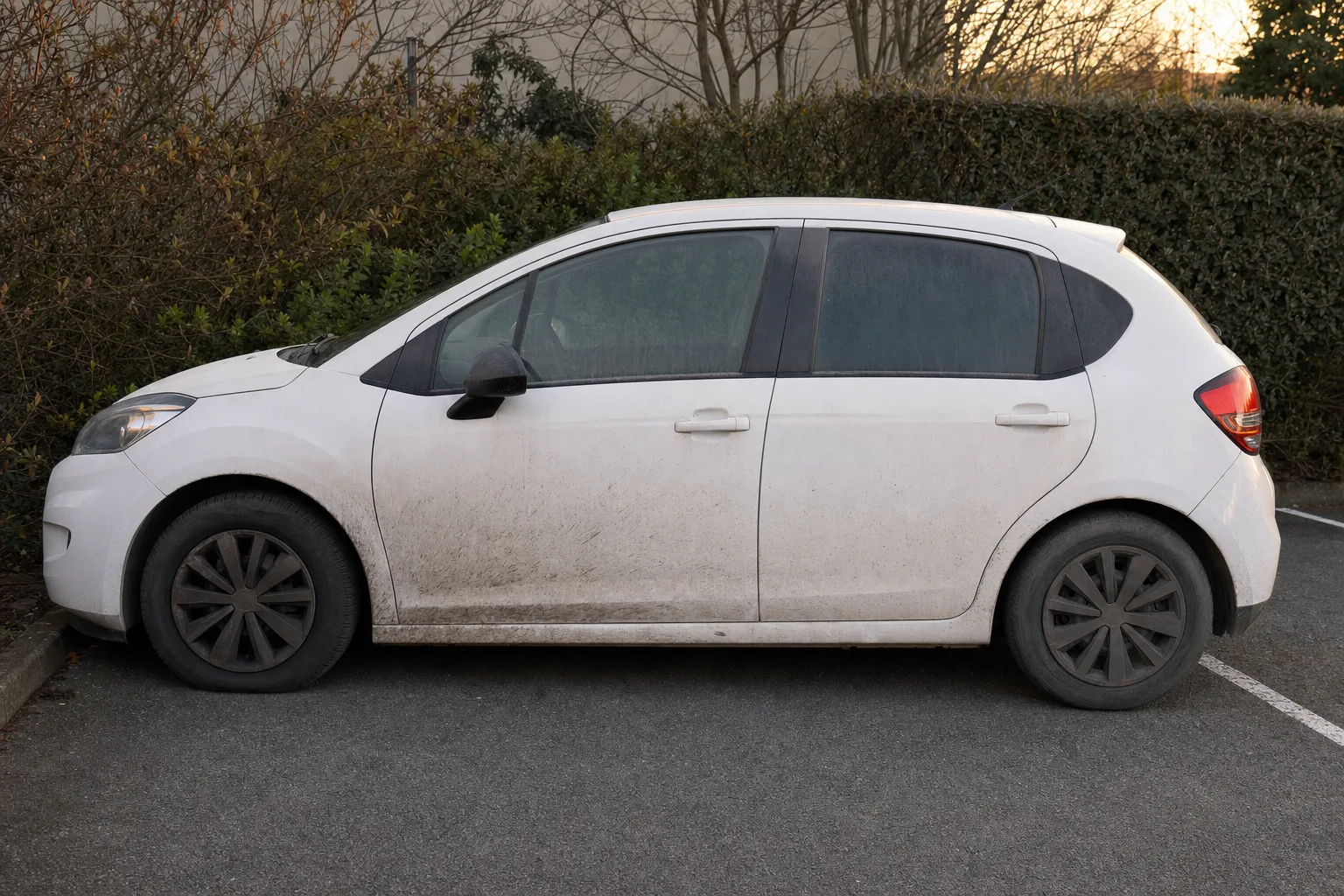 Lavage extérieur de voiture à domicile à Perpignan — flanc avant intervention : carrosserie poussiéreuse, bas de caisse sale, jante noircie.
