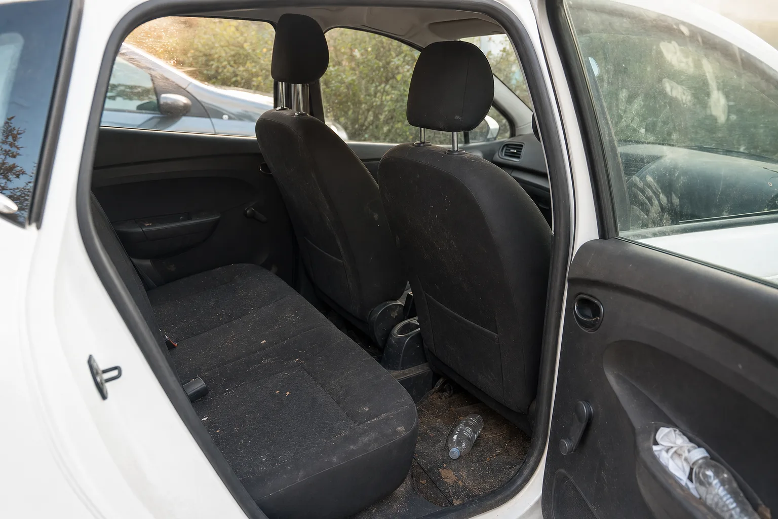 Nettoyage intérieur de voiture à domicile à Perpignan — habitacle avant intervention : sièges en tissu tachés, tapis maculés, déchets au sol.