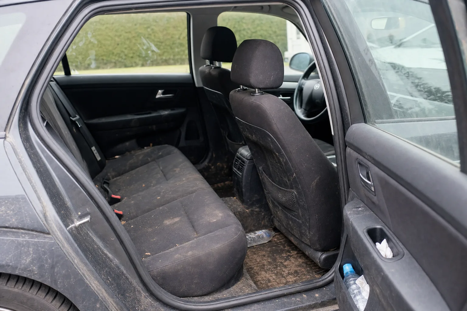 Nettoyage intérieur de voiture à domicile à Strasbourg — habitacle avant intervention : sièges en tissu tachés, tapis maculés, déchets au sol.
