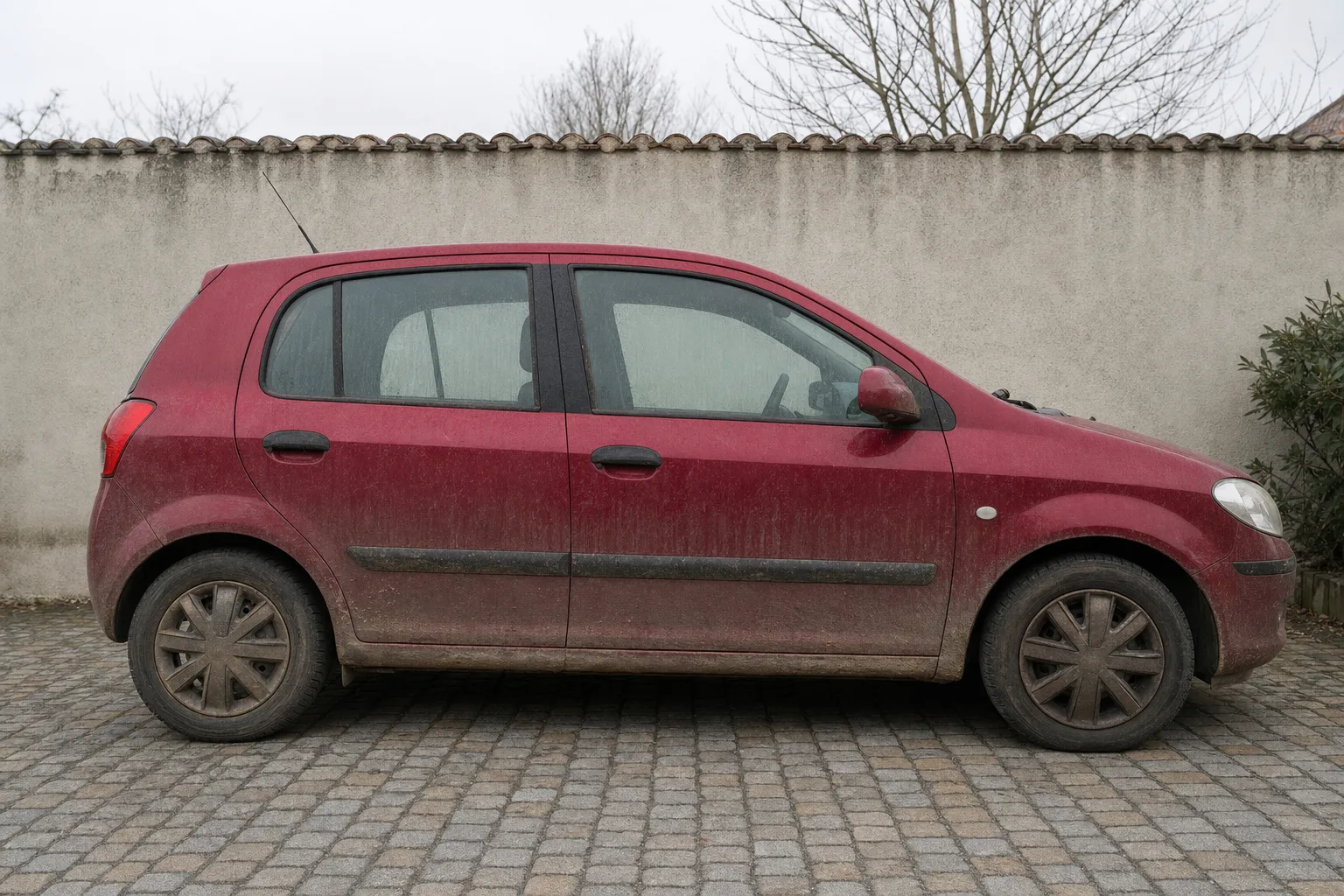 Lavage extérieur de voiture à domicile à Rouen — flanc avant intervention : carrosserie poussiéreuse, bas de caisse sale, jante noircie.