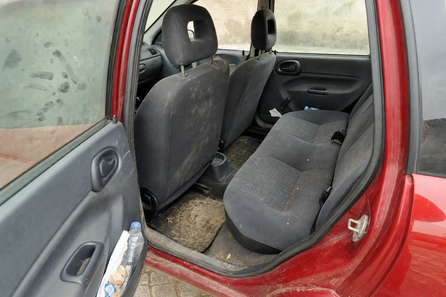 Nettoyage intérieur de voiture à domicile à Rouen — habitacle avant intervention : sièges en tissu tachés, tapis maculés, déchets au sol.