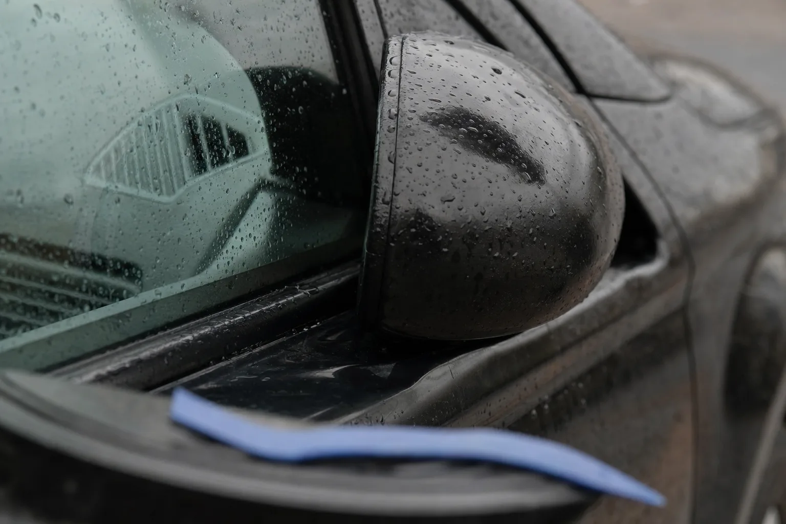 Rétroviseur extérieur resté replié contre la vitre d'une portière, gouttes de pluie sur la coque.